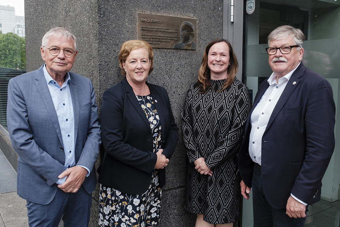 Vier Personen stehen vor Gedenktafel von Erich Kuttner