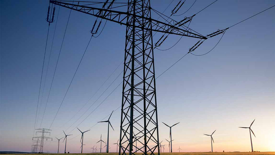 Feld mit Stromleitungen, im Hintergrund einige Windräder. 