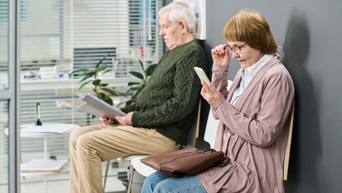 Zwei ältere Patienten sitzen im Warteraum einer Praxis.