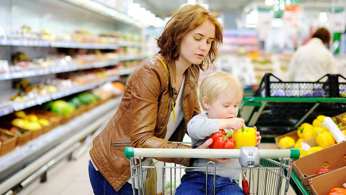 Eine Mutter mit ihrem kleinen Kind im Supermarkt, das Kind hat eine Paprika in der Hand. 
